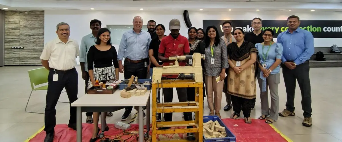 Group of colleagues posing behind a woodworking lathe and tool table in a bright workshop setting like a training area.