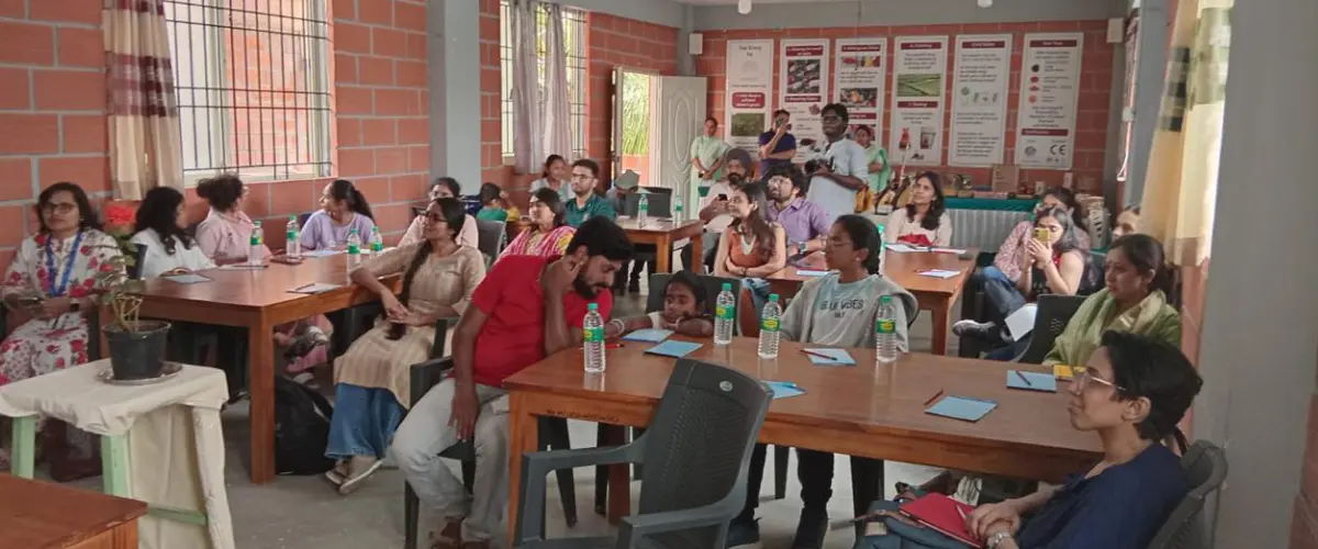 Group of adults in a classroom workshop, seated at tables with water bottles, posters on the wall in the background.