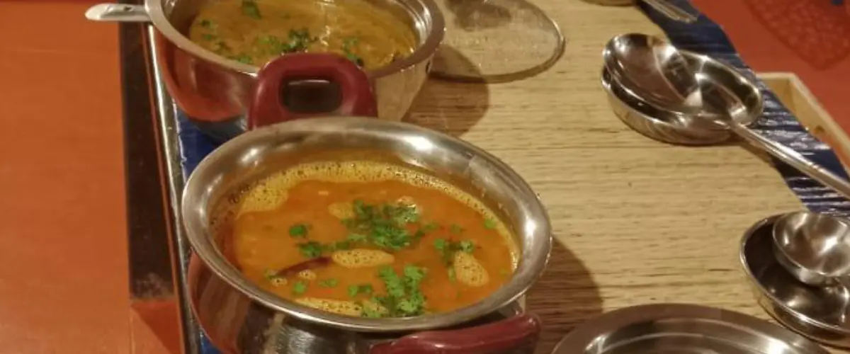 Two curry bowls on a wooden counter, garnished with cilantro, with spoons nearby on the table.