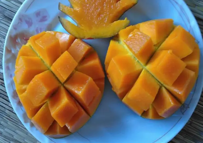 Two ripe mangos cut into cubes on a plate, showcasing bright orange flesh and a decorative mango flower in the background.