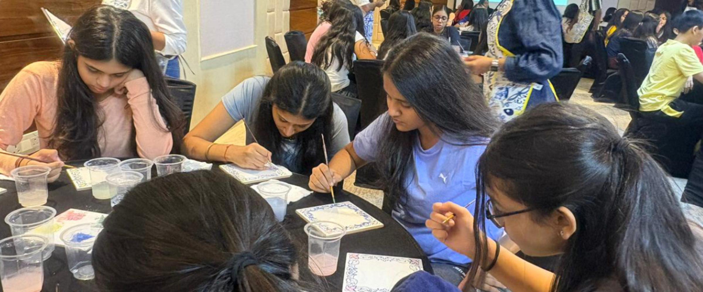 Group of students painting decorative tiles at a table during a workshop.
