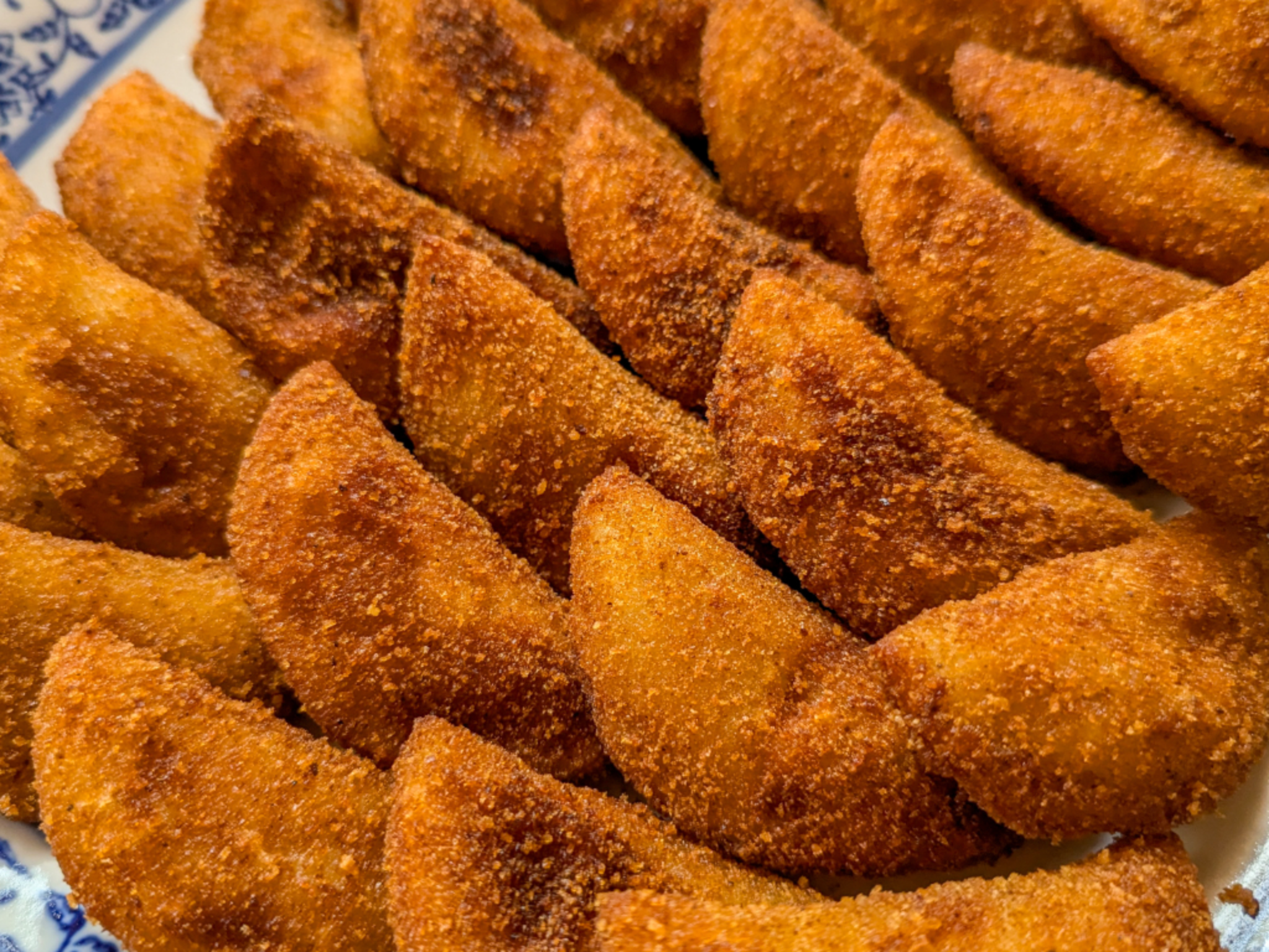 Pile of crispy orange breaded triangular fried bites on a plate with a blue pattern edge.