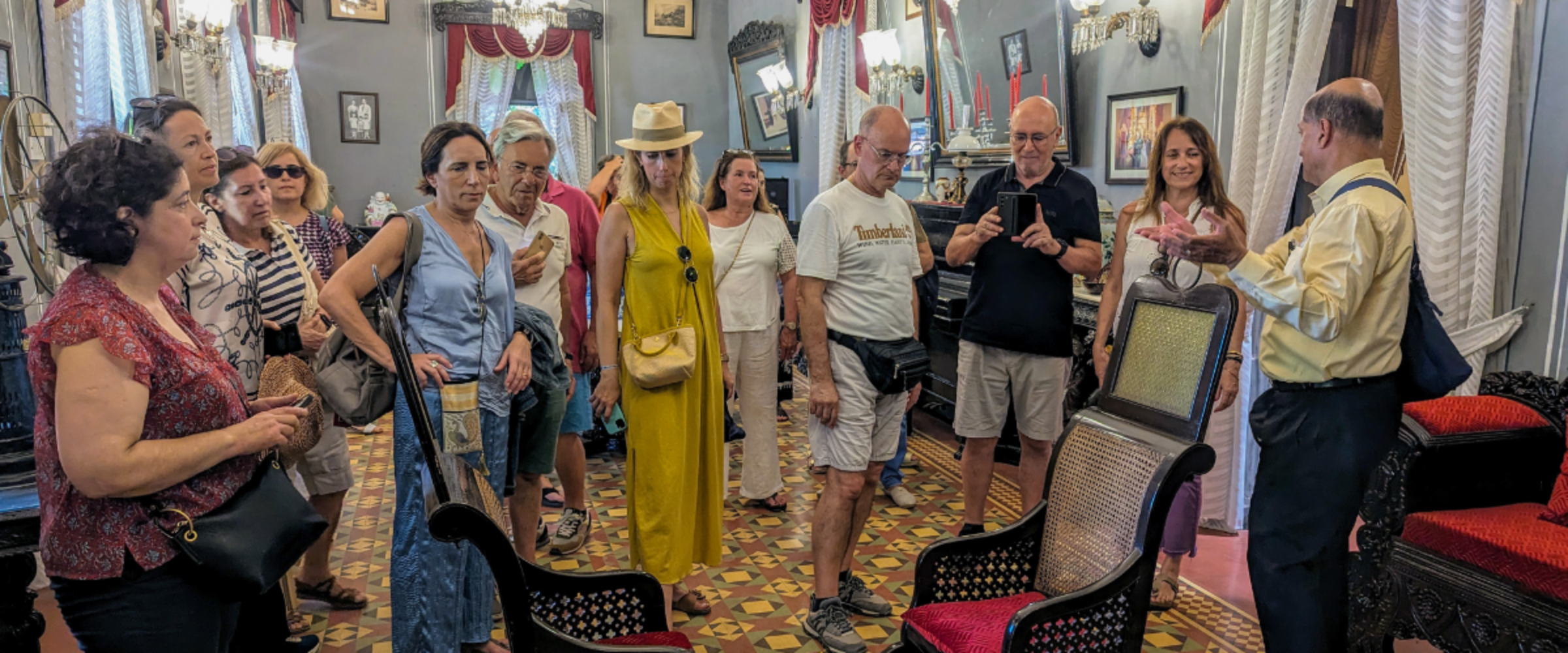 Tour group listening to a guide in a vintage furniture showroom with ornate chairs and patterned floor.