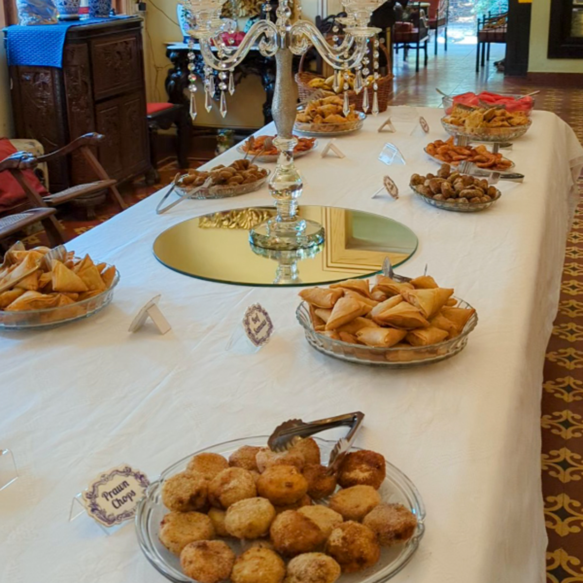 Long banquet table with a white tablecloth, glass bowls of pastries, and a crystal chandelier centerpiece in a dining room.