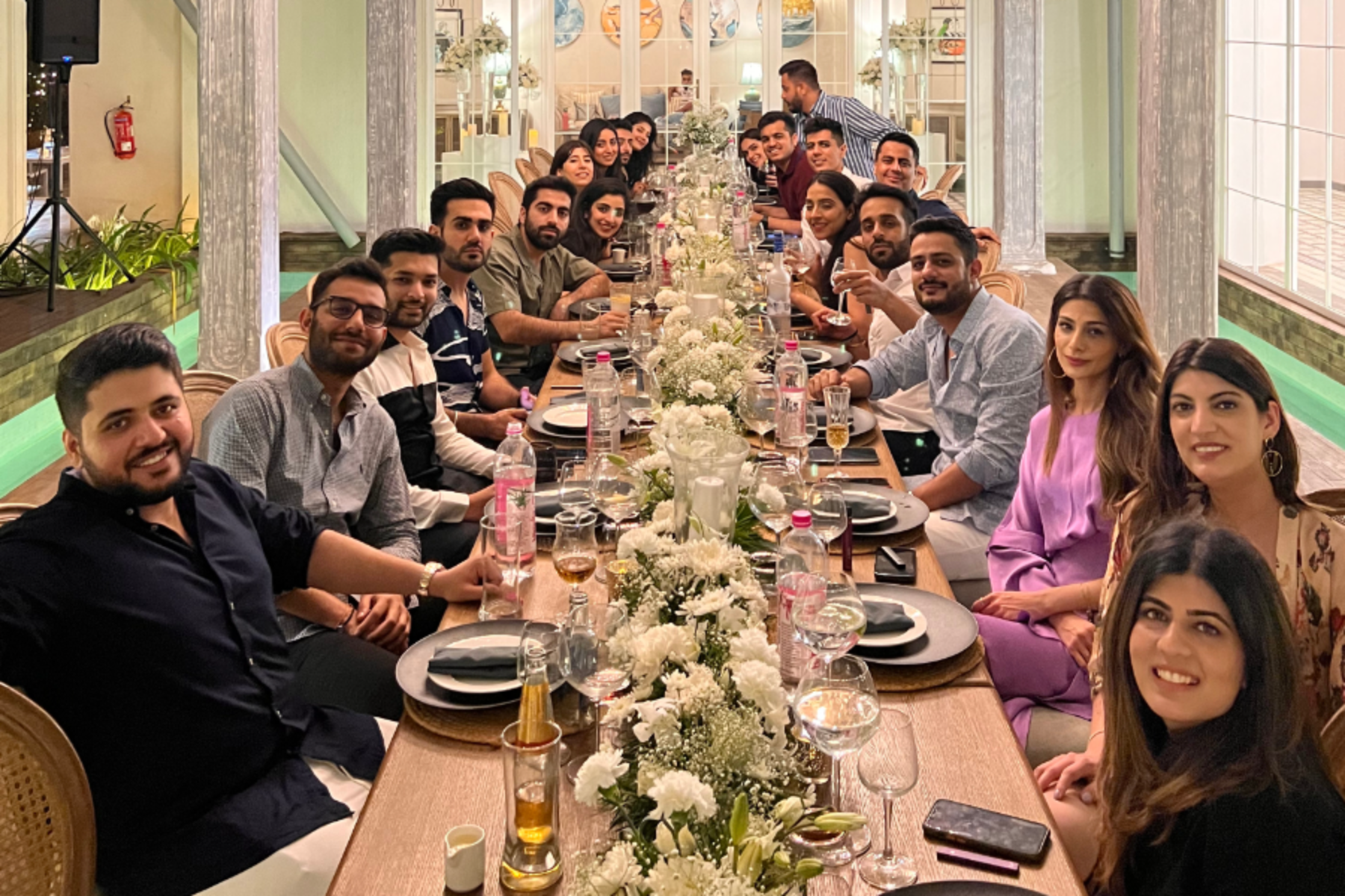 Large group of people seated along a long restaurant table, posing for a group photo during a celebration dinner.