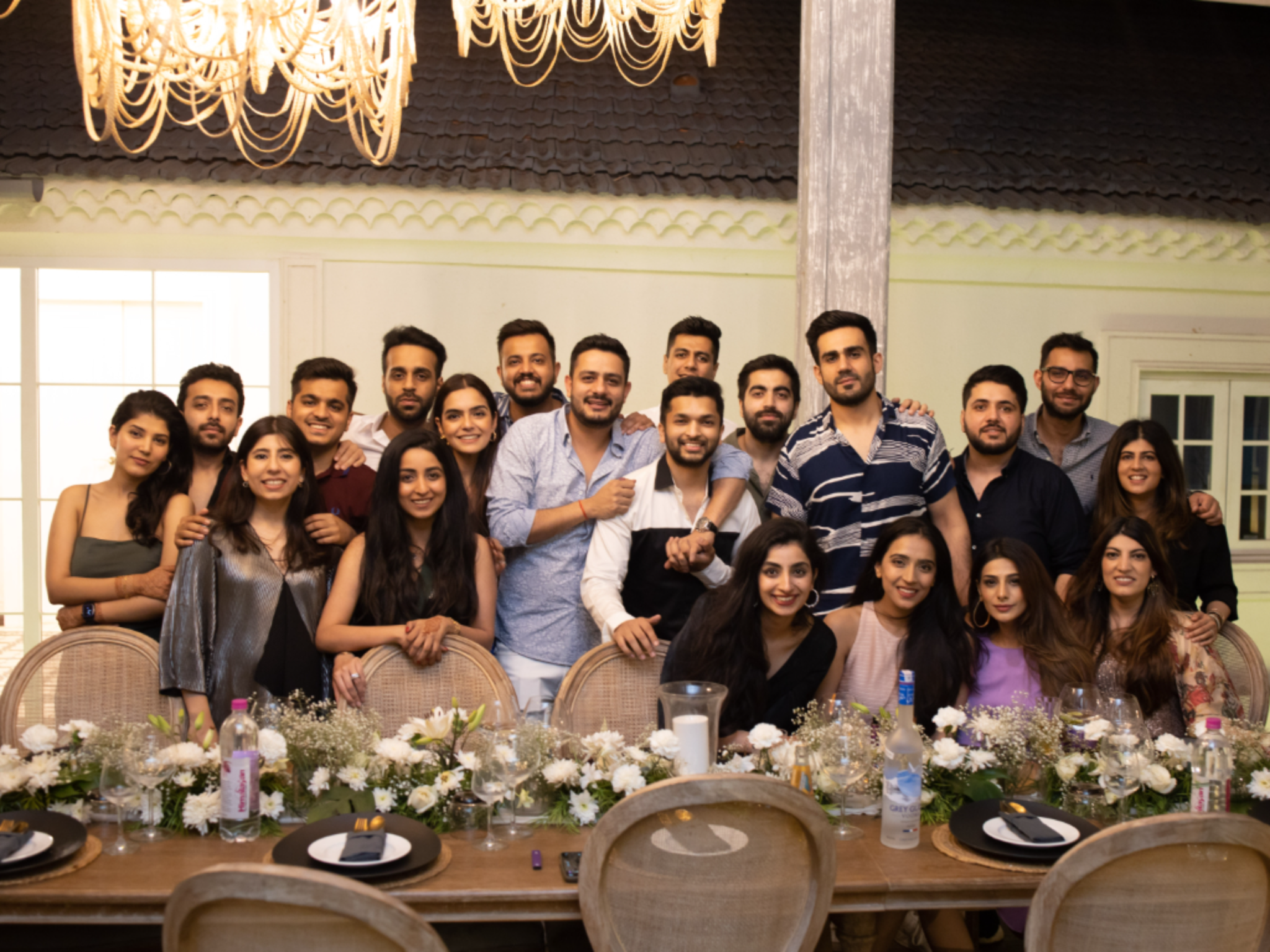 Group of friends posing for a photo at a long dining table with floral centerpieces and place settings in a bright indoor room