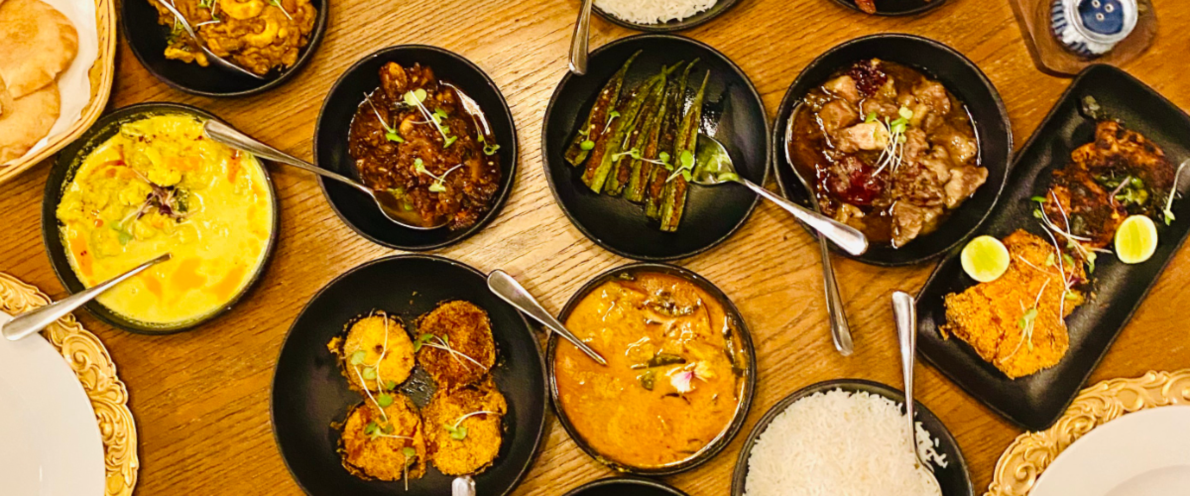 A top-down view of a shared table with many bowls of curry, fried items, rice, and vegetables arranged for a feast.