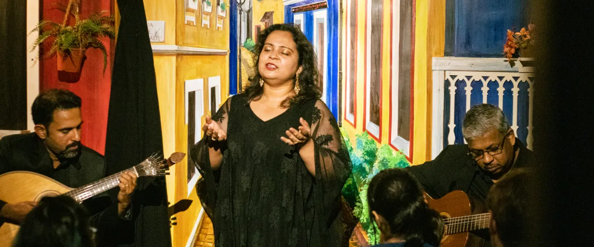 Female singer with two guitarists in a small venue, vibrant mural walls behind them.