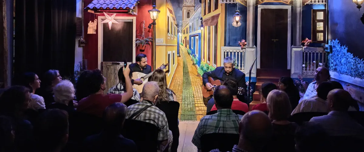 Two guitarists performing for an audience in a colorful mural-clad venue with a painted alley backdrop, center stage left and right.
