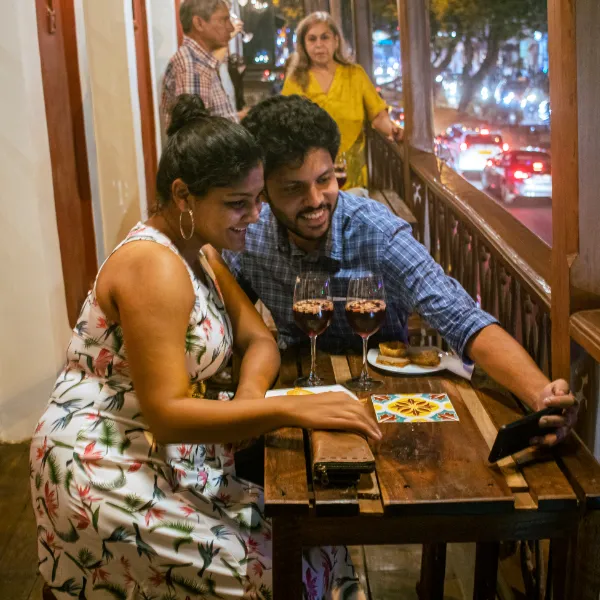 Couple at a wooden table in a restaurant taking a selfie with two glasses of red wine and a dessert plate nearby in a cozy setting.