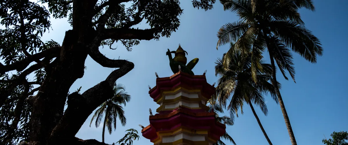 Colorful multi-tiered pagoda rising between palm trees against a bright blue sky.