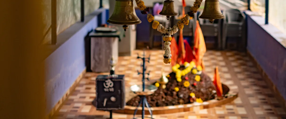 Interior Hindu shrine with hanging bells and a flower-adorned altar in a tiled room.