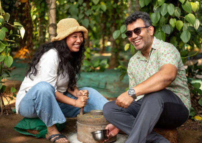 Two people in a garden laughing while using a stone mortar and pestle together.