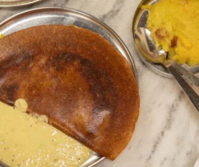 Masala dosa on a metal plate with coconut chutney on the side and potato curry nearby on a marble table